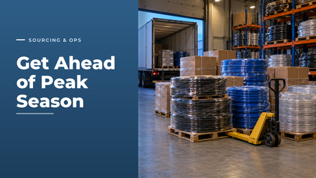 Goods-in bay of a hose distributor at dawn with pallets of shrink-wrapped black, blue and clear hose coils being unloaded from a lorry beside stocked pallet racking