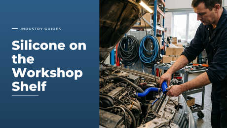Workshop technician in navy overalls fitting a bright blue silicone coolant hose into an open engine bay, with coiled hose on the wall behind