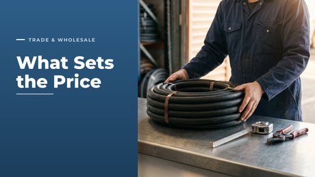 Warehouse worker lowering a banded coil of black rubber hose onto a stainless steel trade counter, with a tape measure and hose cutter alongside